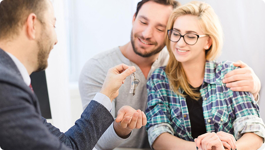 Asesor inmobiliario entregando las llaves de una vivienda a una pareja sonriente, simbolizando la compra o alquiler de una casa.