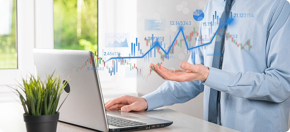 Mano sosteniendo unos gráficos ascendentes de color azul y un portátil abierto