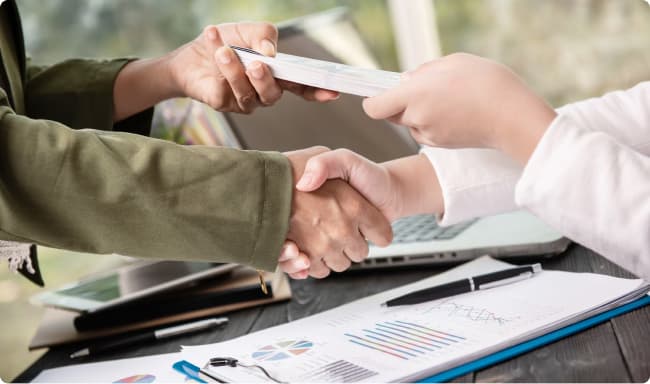 Un hombre y una mujer estrechando la mano mientras intercambian un taco de papeles