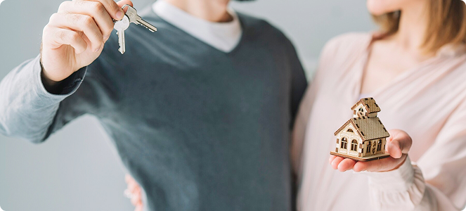 Hombre sosteniendo un manojo de llaves y mujer sujetando una casa en miniatura mientras ambos sonríen.
