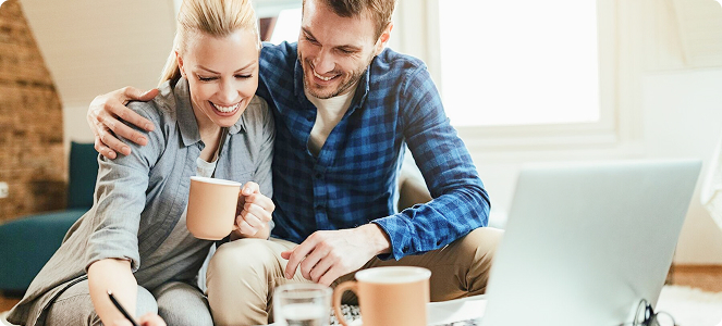 Pareja sonriendo mientras revisa documentos en una mesa con tazas de café.