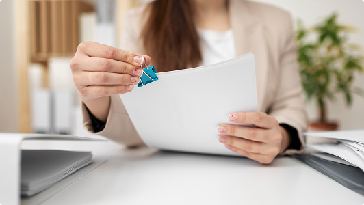 Persona sujetando un conjunto de documentos sujetos con un clip azul en un escritorio.