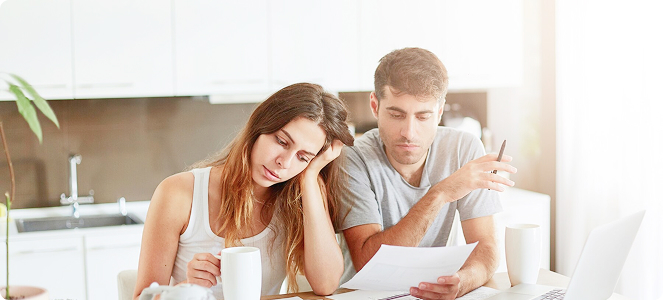 Pareja sentada en la mesa de la cocina revisando documentos junto a un ordenador portátil.