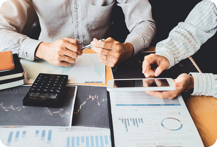 Dos personas analizando gráficos financieros en documentos, con una calculadora y una tablet sobre la mesa.